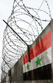 Barbwire and grey wall with Syria national flag